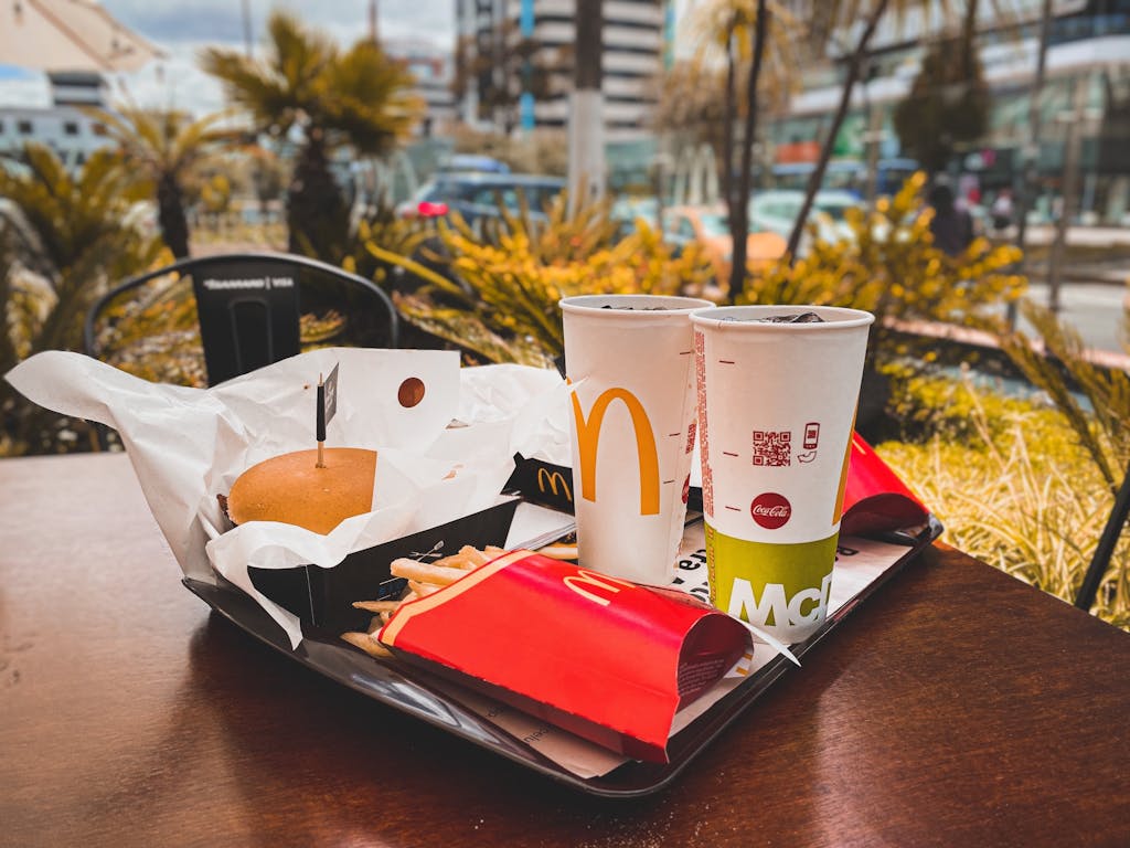 An appetizing fast food meal with burger, french fries and drinks on an outdoor table in an urban setting.
