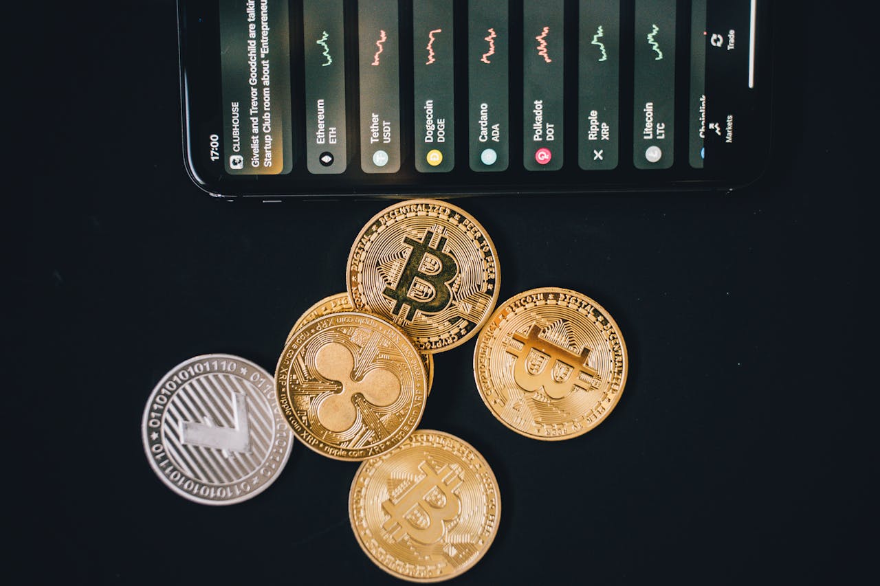 Smartphone with cryptocurrency market data and physical coins on a black surface, representing the method of bringing money to Russia in crypto