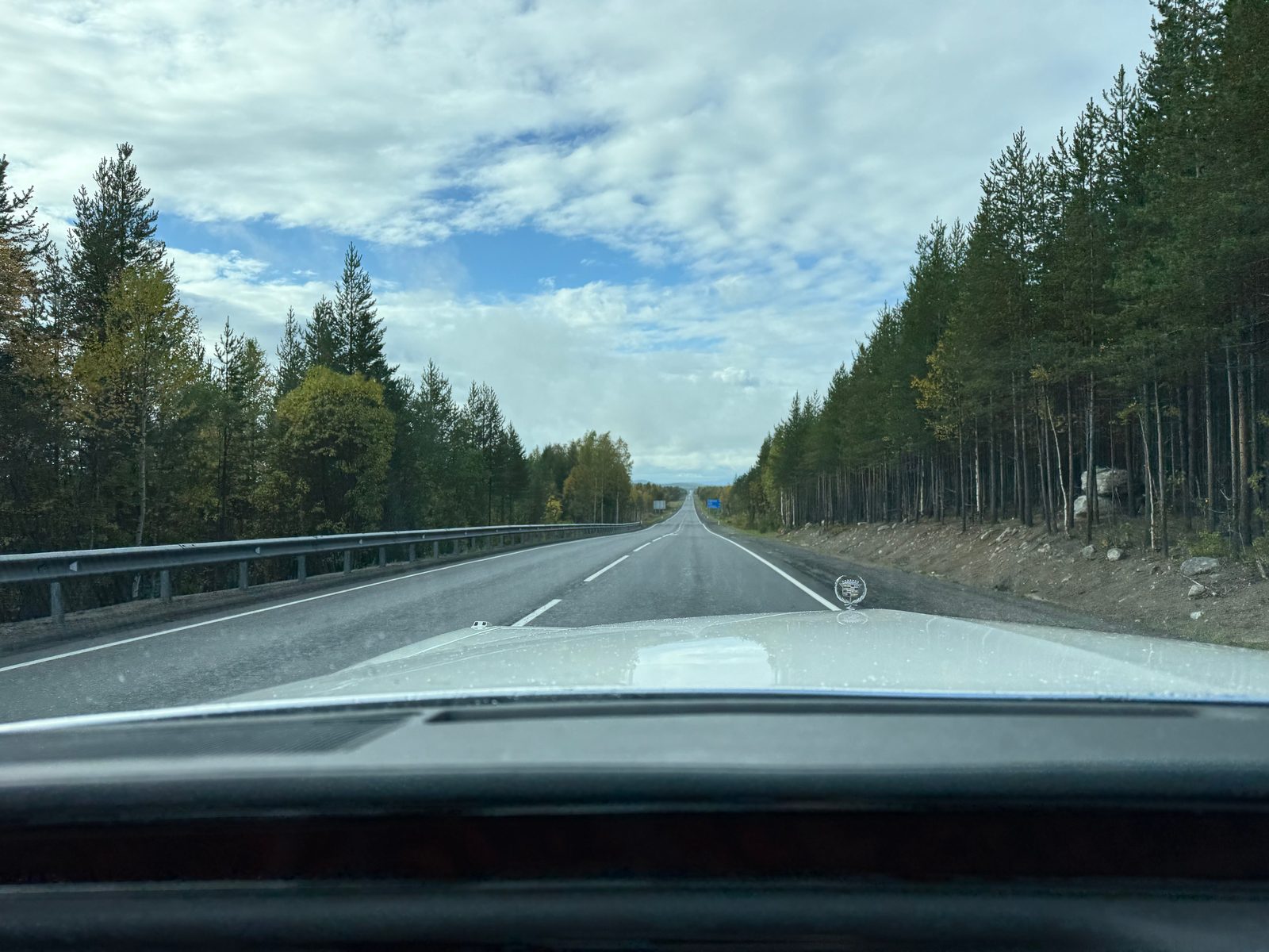 Empty Russian road through pine forest seen from the bonnet of a Cadillac Brougham