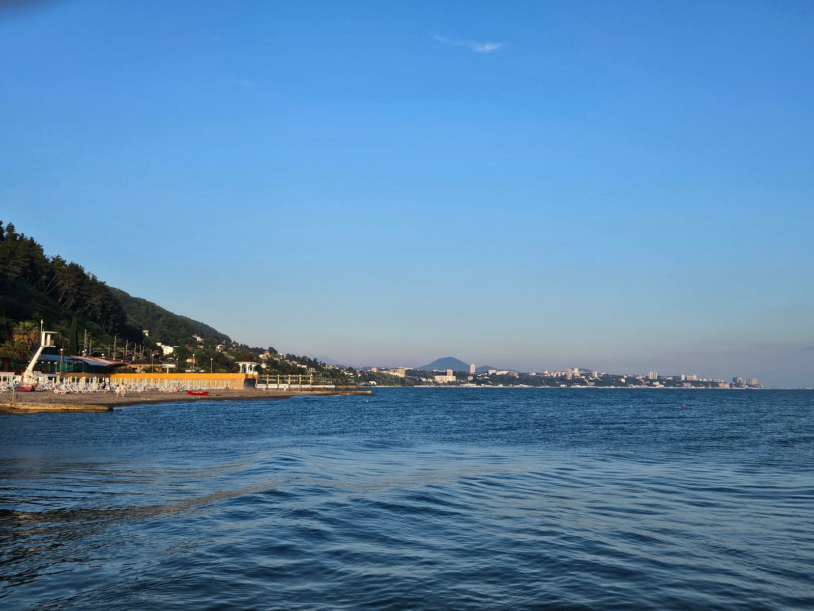View of the Sochi coastline from the sea, with green hills and the city in the background