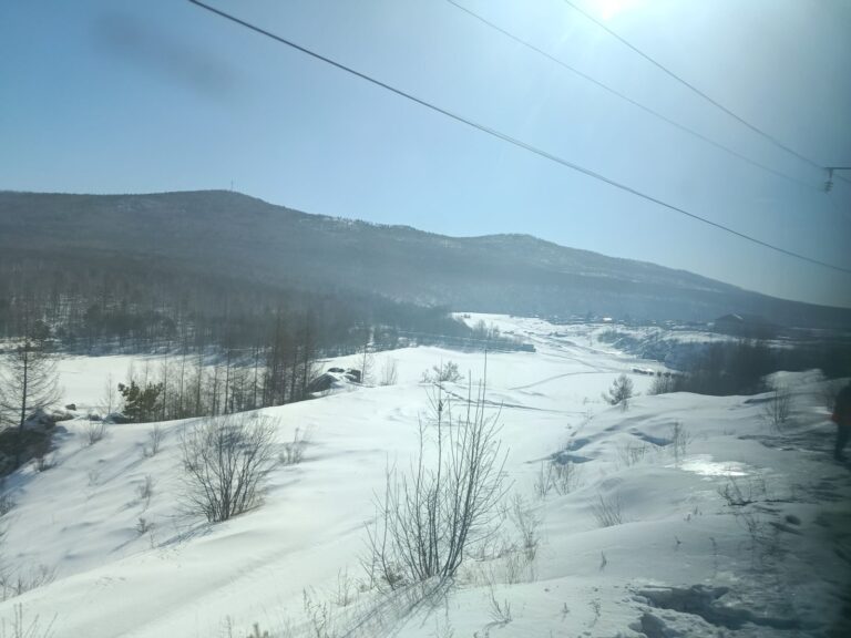 Wooded hills and snowfields under a blue sky, seen from the Trans-Siberian window